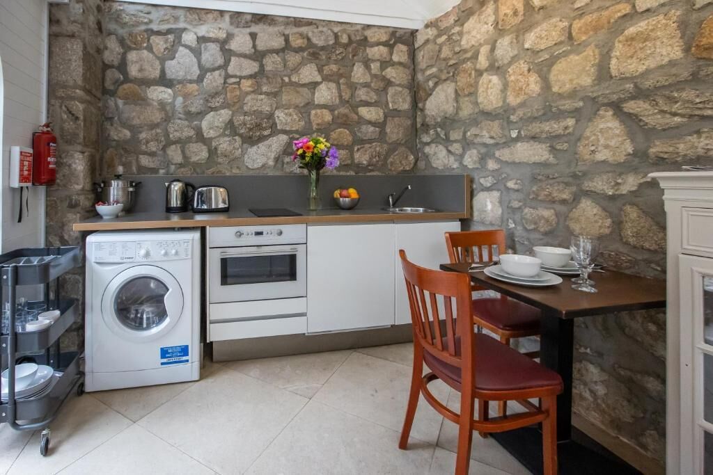 A compact kitchen with a stone wall, a washing machine, a stove, and a dining area with a table and chairs.