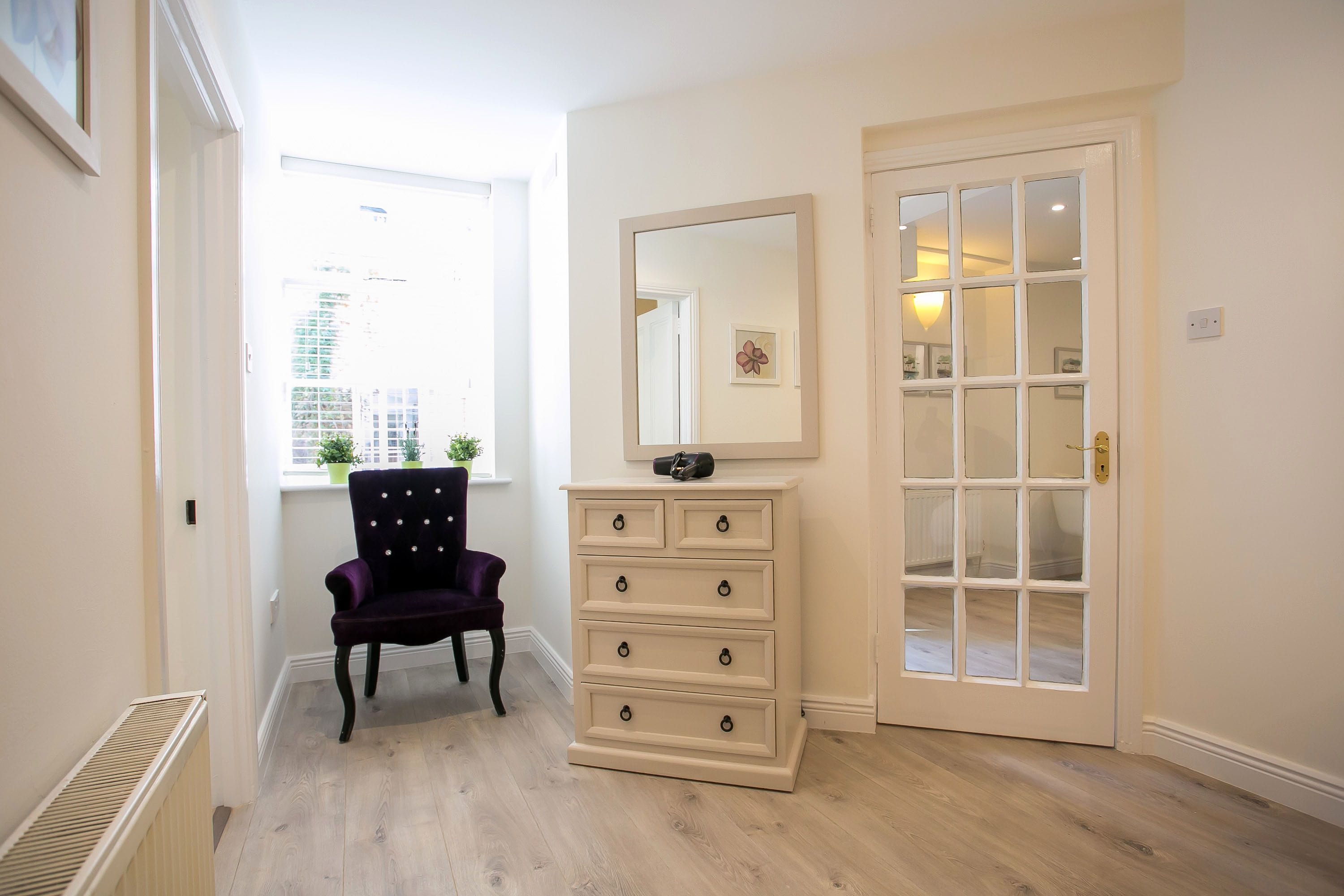 A hallway with a radiator, a chair, a dresser with drawers, a mirror, and a door with glass panels.