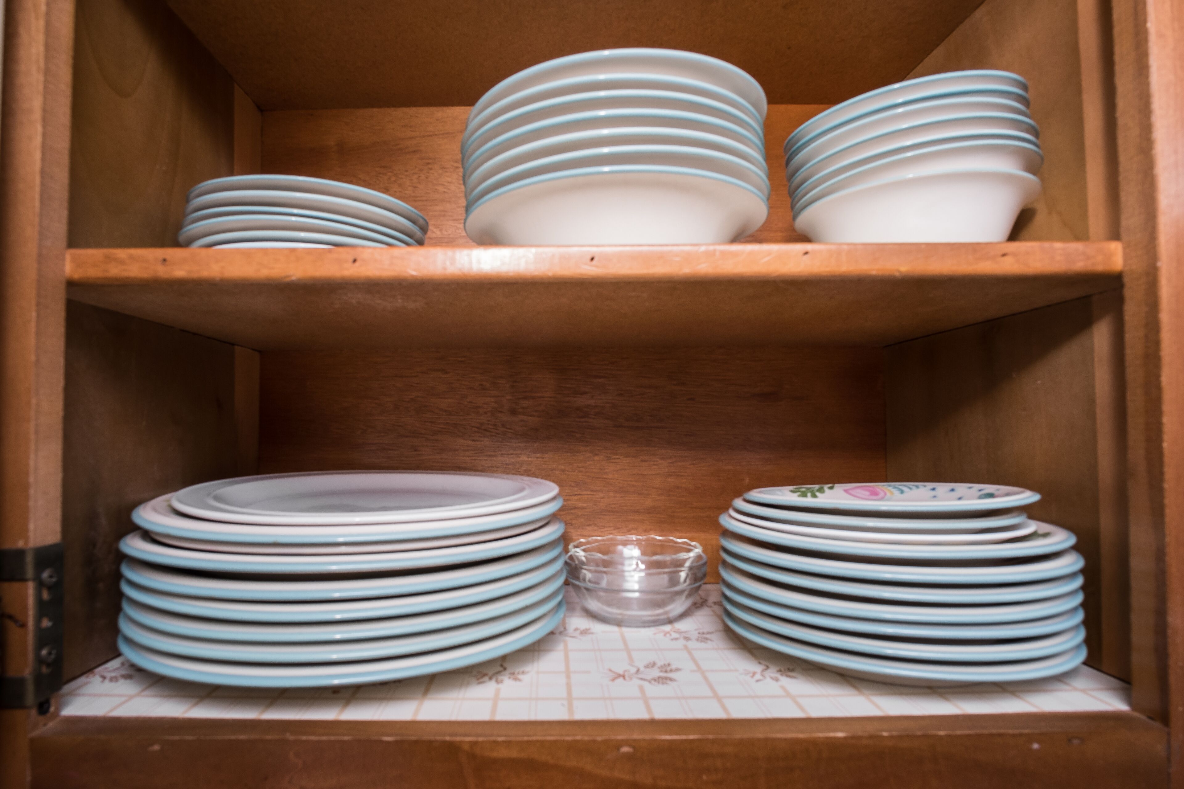 A wooden cabinet with multiple shelves holding stacks of plates and a small glass bowl.