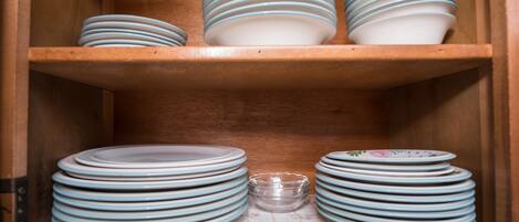 A wooden cabinet with multiple shelves holding stacks of plates and a small glass bowl.