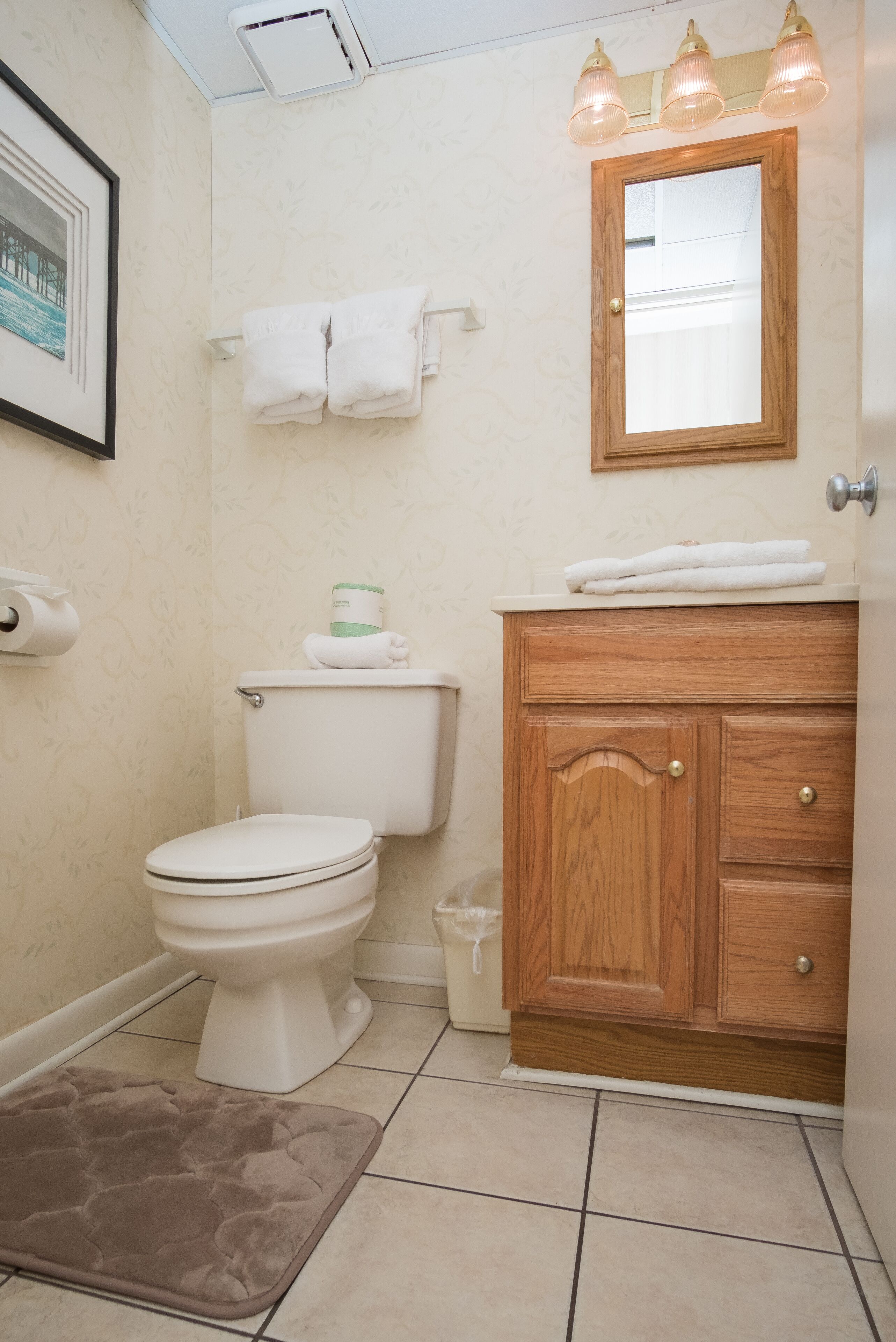 A bathroom with a toilet, a wooden vanity with a mirror, and a framed picture on the wall.
