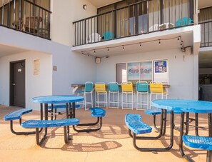 A courtyard with blue tables and chairs, a balcony with a railing, and a sign for 'Sand Bar'. - Scenic Ocean front first floor pool view spacius condo for up to 4 adults. (Garden City)