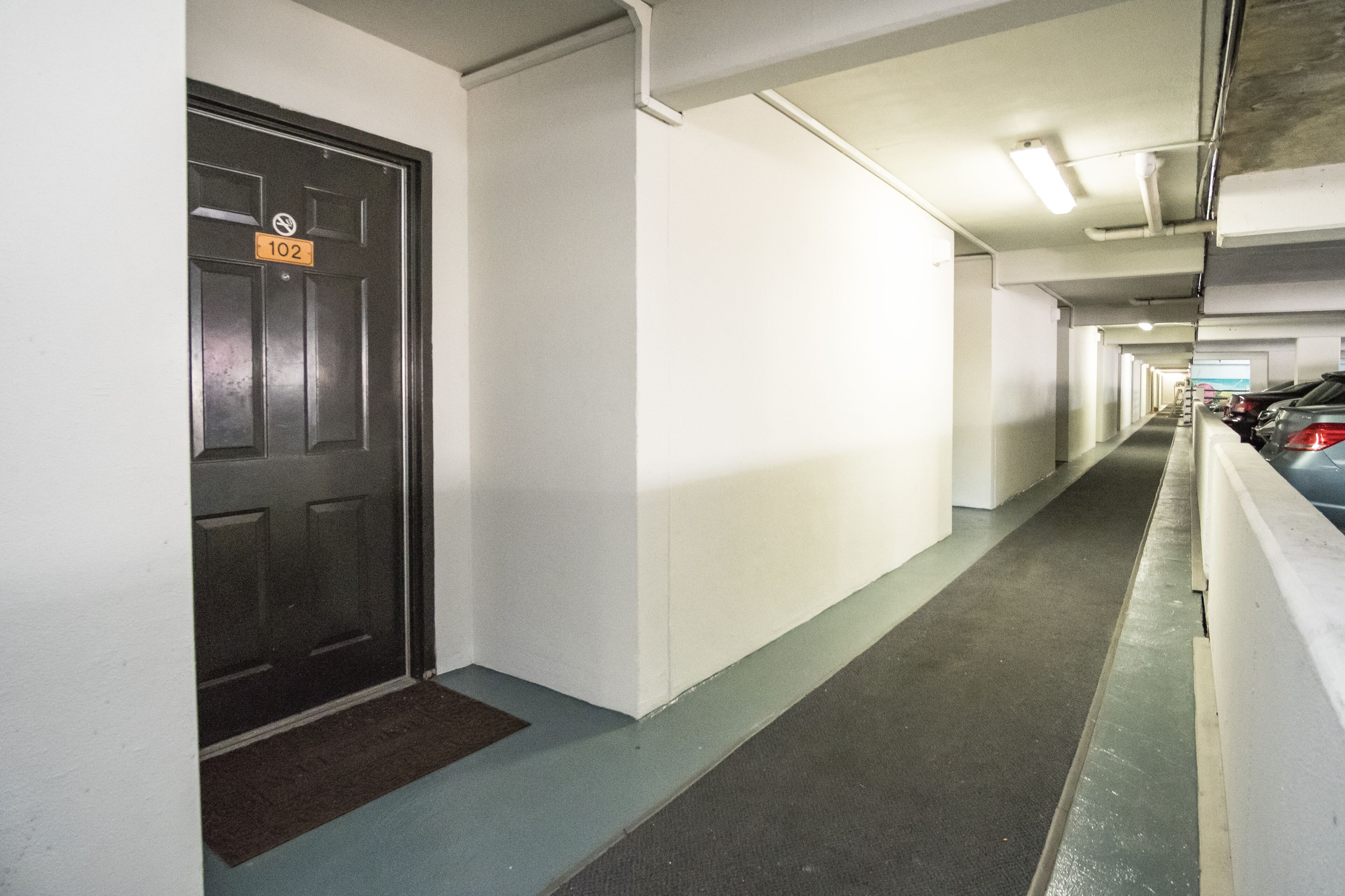 A parking garage corridor with a door marked "102" and a doormat.