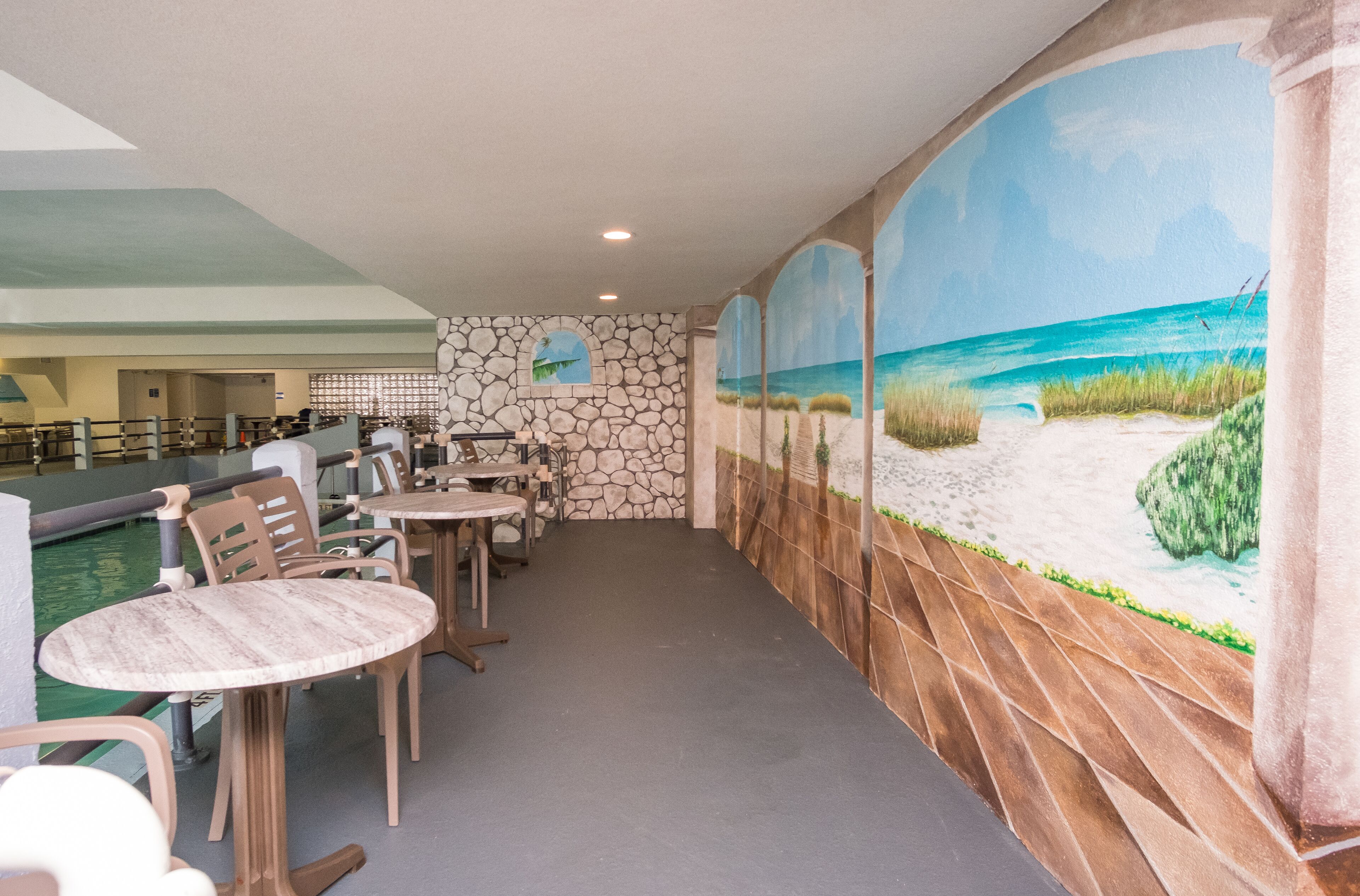 Ein Restaurant mit Außenbereich, Steinwänden und einer Wandmalerei mit Strandmotiv.