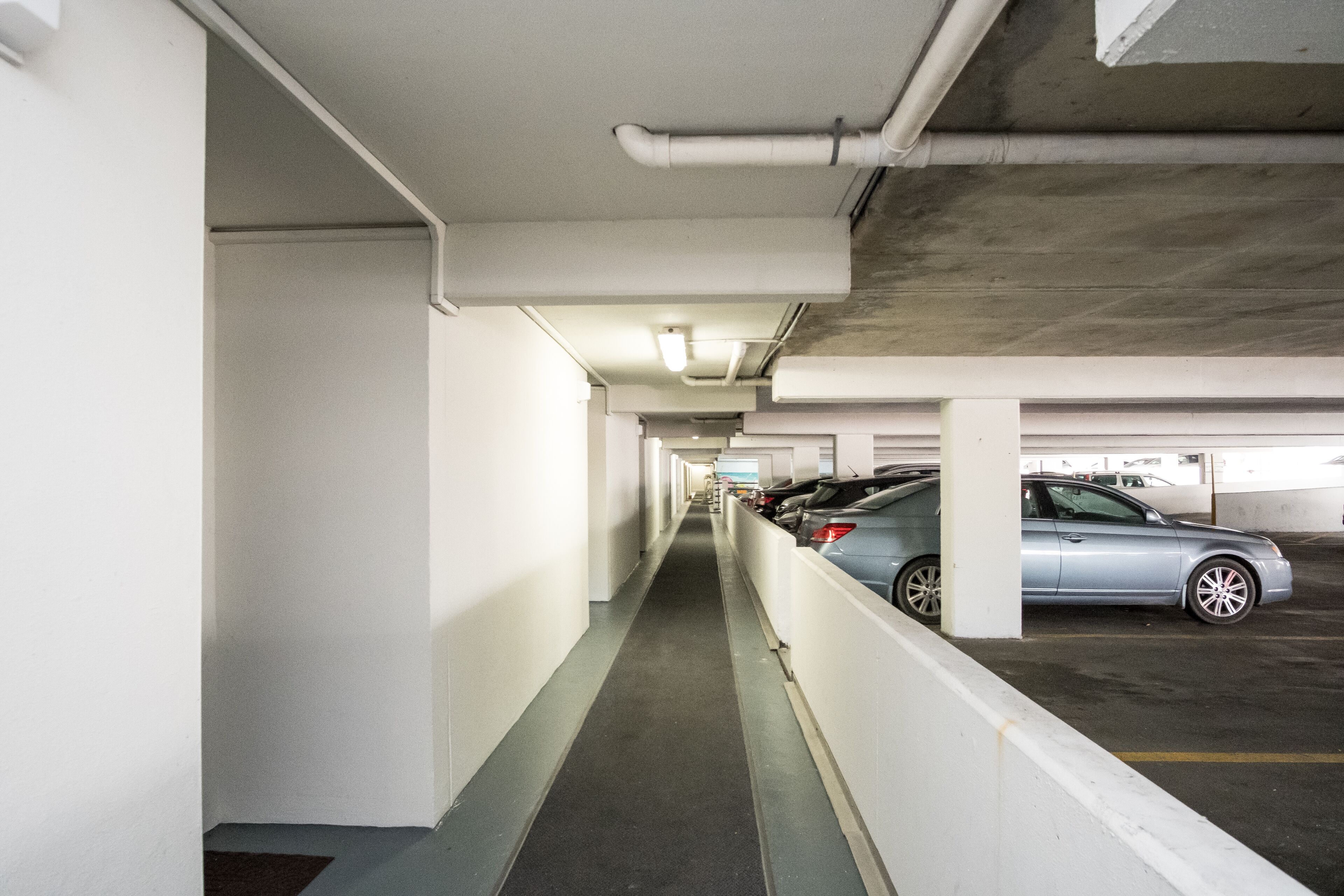 Un parking avec un plafond en béton, des murs blancs et une passerelle.