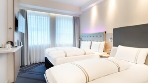 Hotellihuone, jossa on kaksi sänkyä, televisio, työpöytä, jossa on kahvinkeitin, ja ikkuna, jossa on verhot.