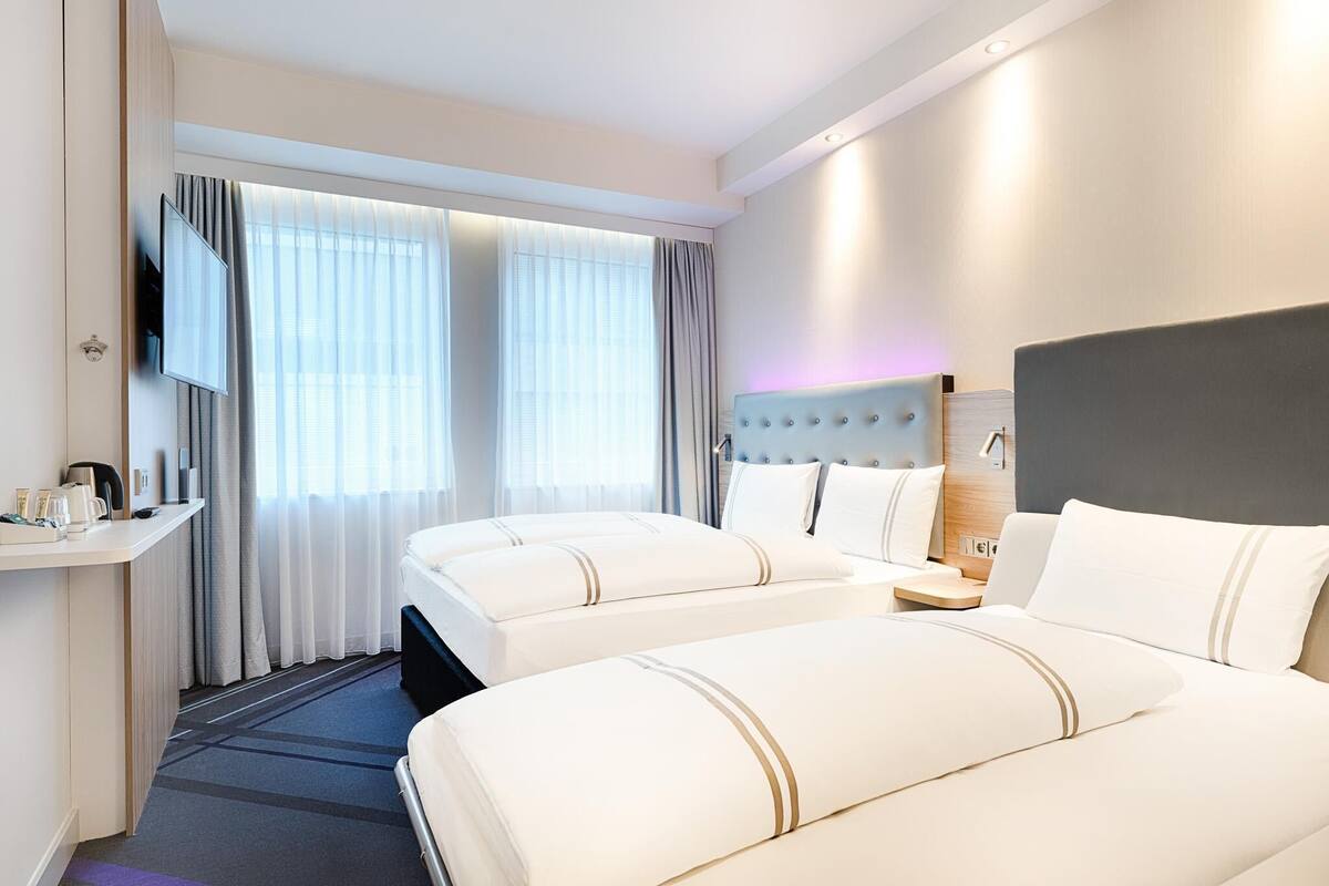A hotel room with two beds, a TV, a desk with a coffee maker, and a window with curtains.