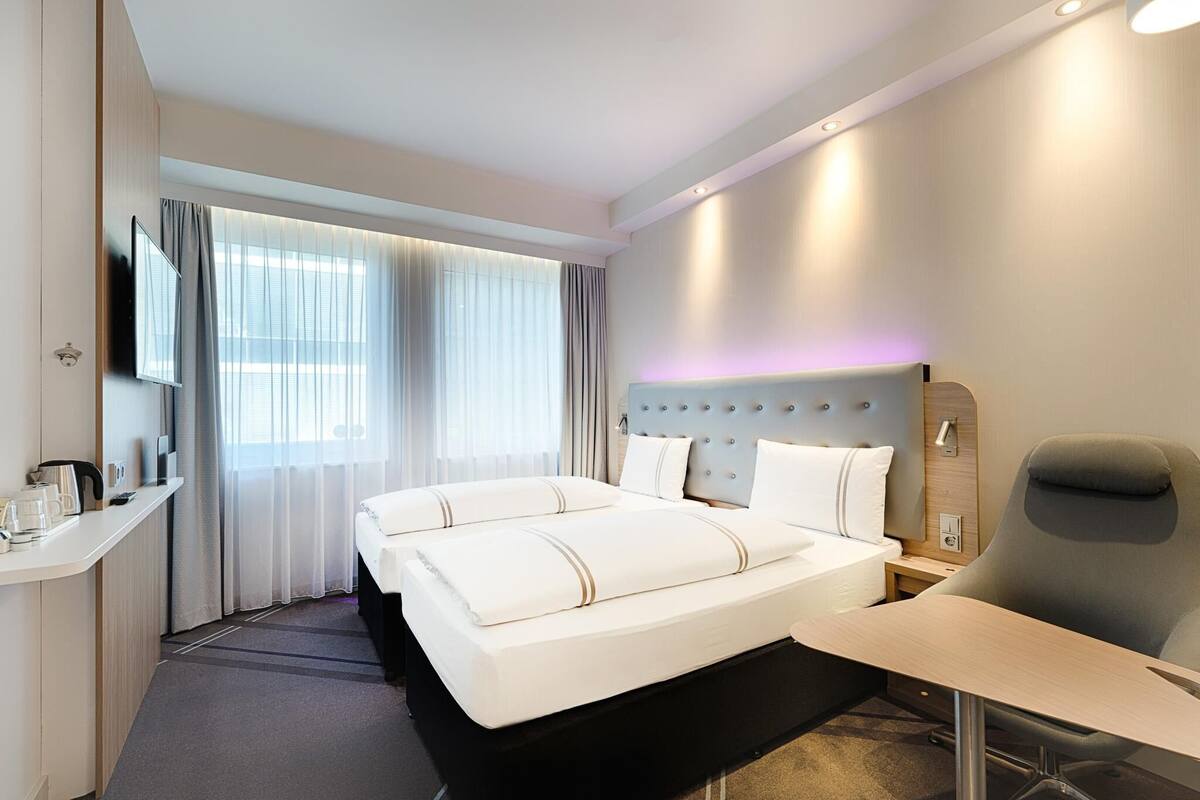 A hotel room with a double bed, a desk, a chair, a TV, and a window with curtains.