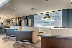 Een hotel receptie in modern design, met een receptiebalie met de naam 'Premier Inn', een grote muur met inspirerende citaten, en een goed verlicht interieur.