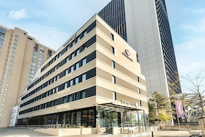 Ein Hotel mit modernem Design, das eine markante Eingangszone mit Überdachung und sichtbarer Beschilderung zeigt.