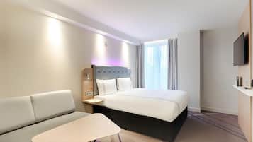 A hotel room with a bed, a sofa, a small table, a TV, and a window with curtains.