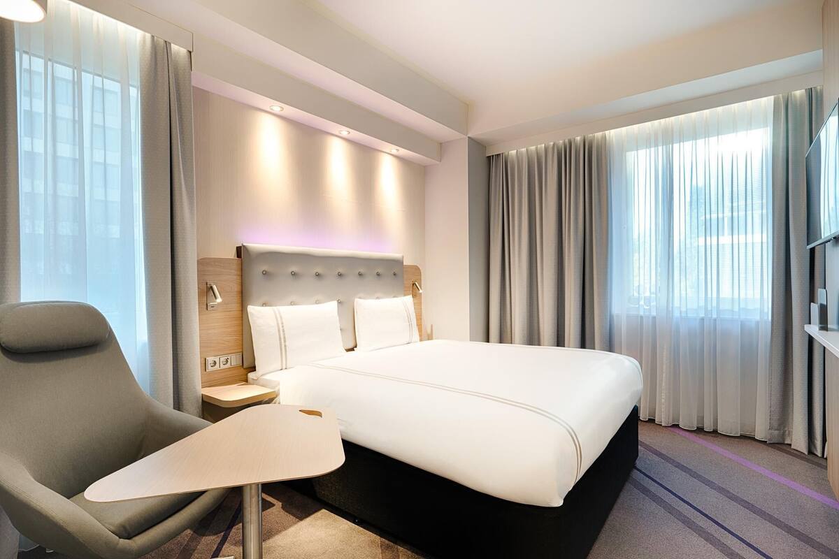 A hotel room with a bed, a chair, a small table, a nightstand, and a TV.