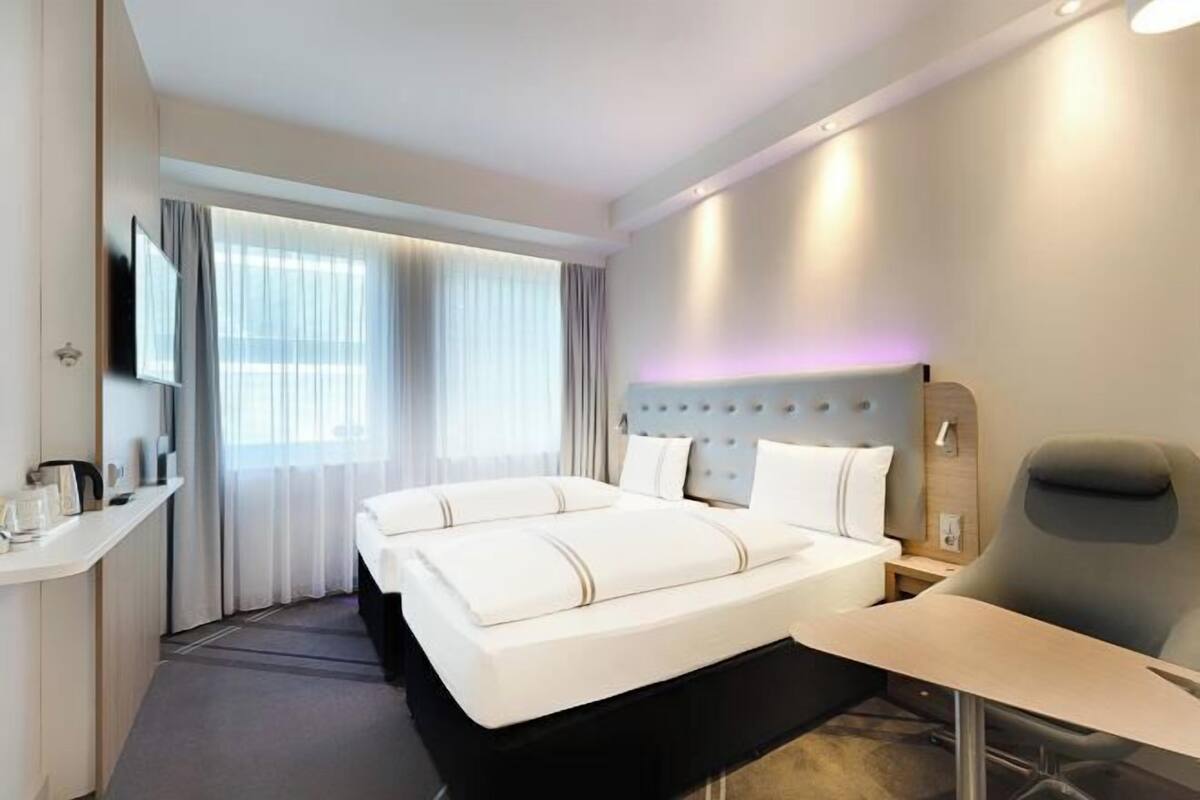 A hotel room with a large bed, a desk, a chair, a television, and a window with curtains.