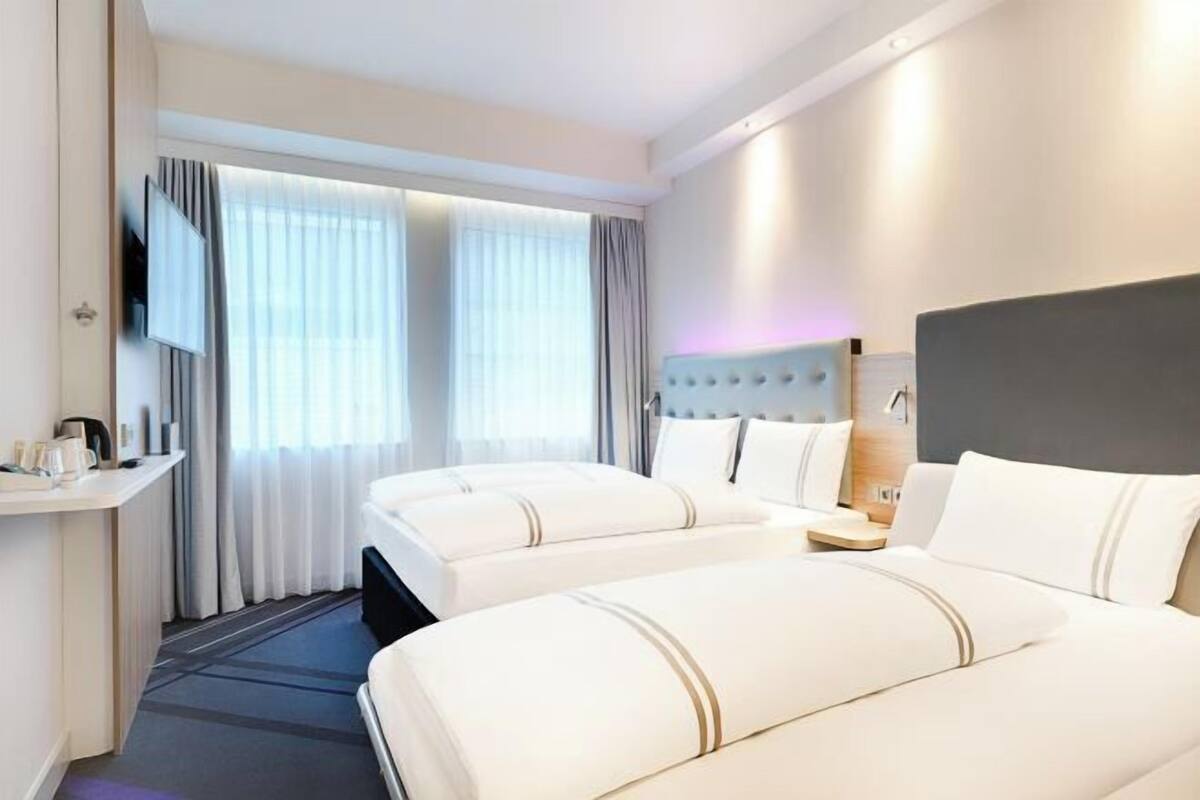 A hotel room with two beds, a TV, a bedside table, and a window with curtains.