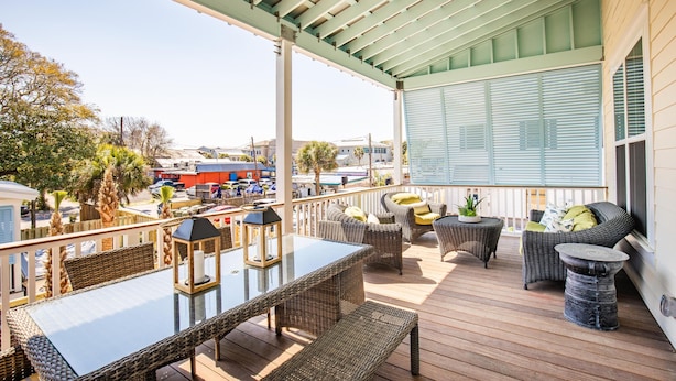 A covered outdoor patio with wicker furniture, a glass-top table, and a view of the surrounding area.