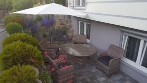 Een terras met rieten meubels, een ronde tafel en een witte parasol.