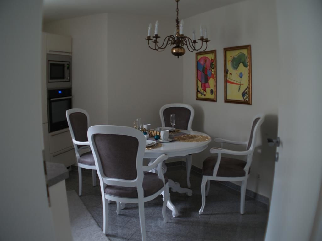 A dining area with a round table, four chairs, a chandelier, and two framed artworks on the wall.