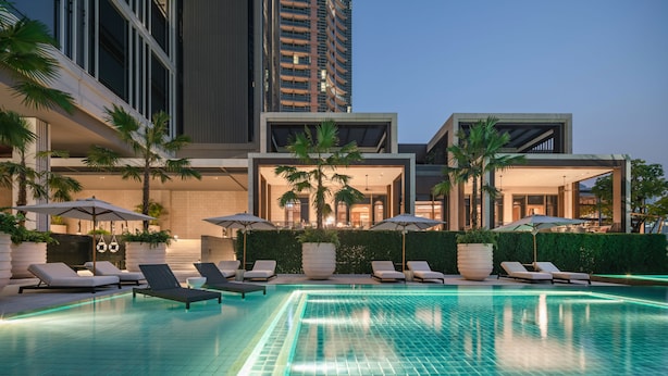 A modern hotel pool area with lounge chairs and umbrellas, surrounded by tall buildings and palm trees. - Four Seasons Hotel Bangkok at Chao Phraya River (Bangkok)