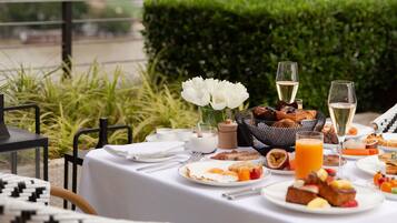A table set for breakfast with a city view, including high-rise buildings and a hedge in the foreground.