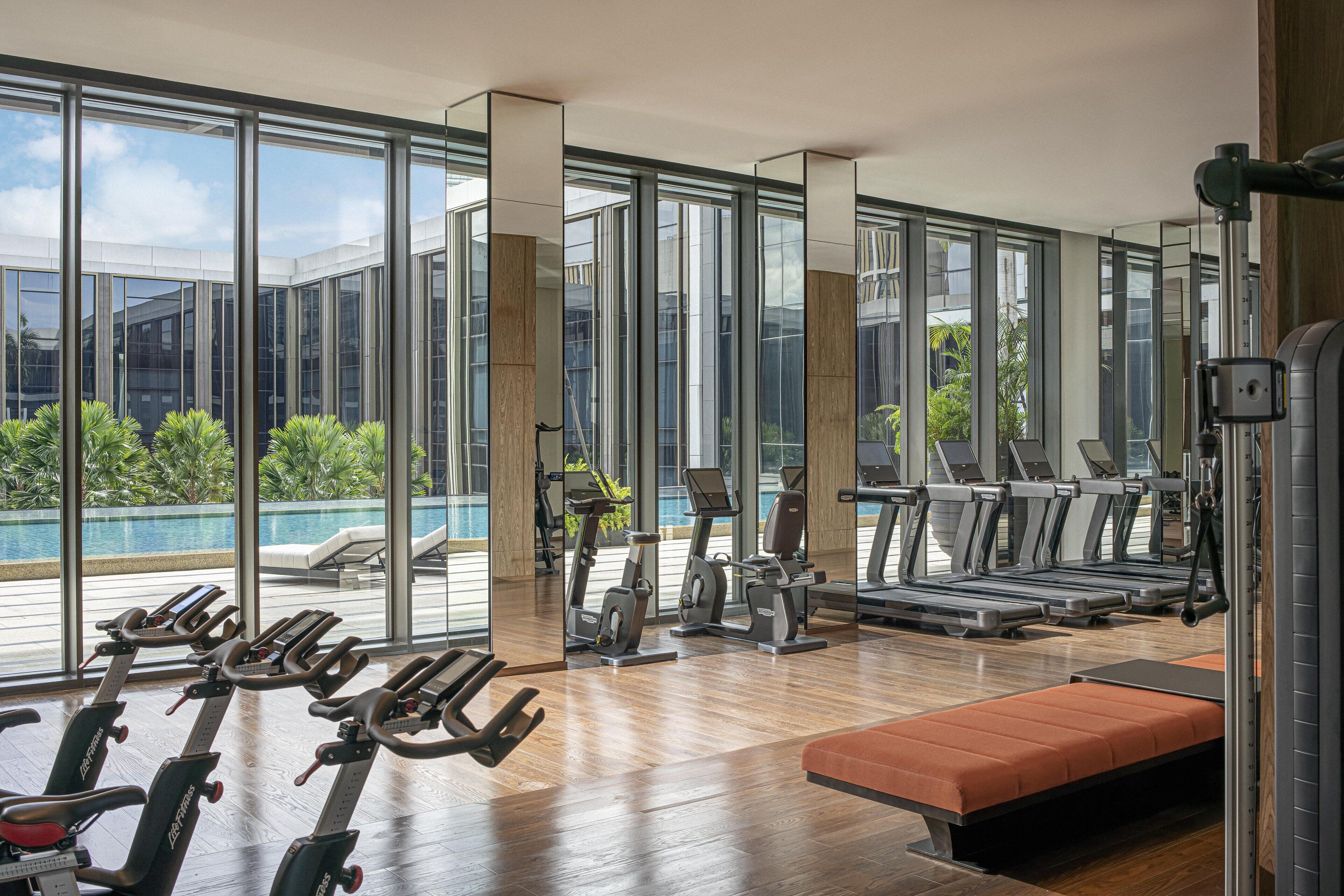 A gym with exercise equipment, a bench, and large windows overlooking a pool.