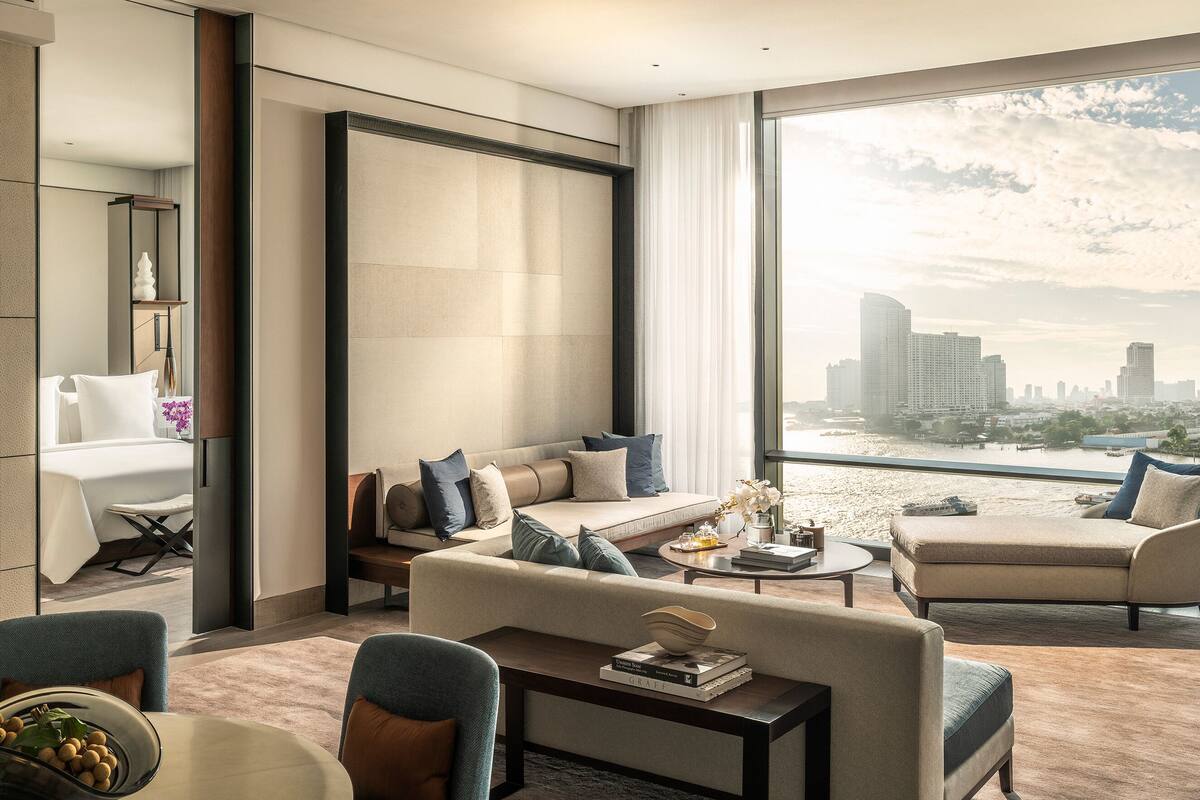 A modern hotel room with a large window offering a city view, a comfortable seating area, and a dining table.