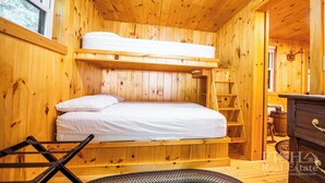 Una habitación tipo cabaña de madera con literas, una escalera, un escritorio pequeño y un aparador.