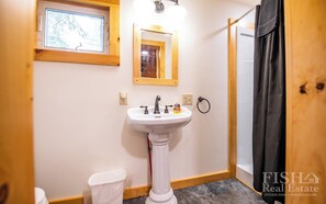 Une salle de bain avec un lavabo sur colonne, un miroir, une fenêtre et un rideau de douche.