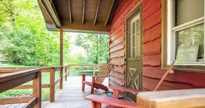 A wooden deck with benches and a chair, overlooking a forested area.
