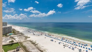 Ein Strand mit einer Reihe blauer Sonnenschirme und einem Hotelgebäude im Hintergrund.
