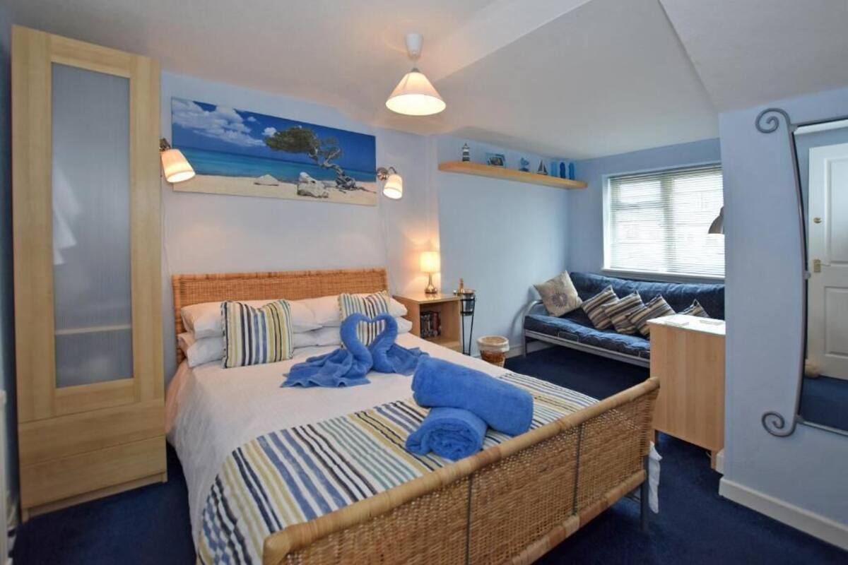 A bedroom with a bed, a sofa, a window, and a painting on the wall.