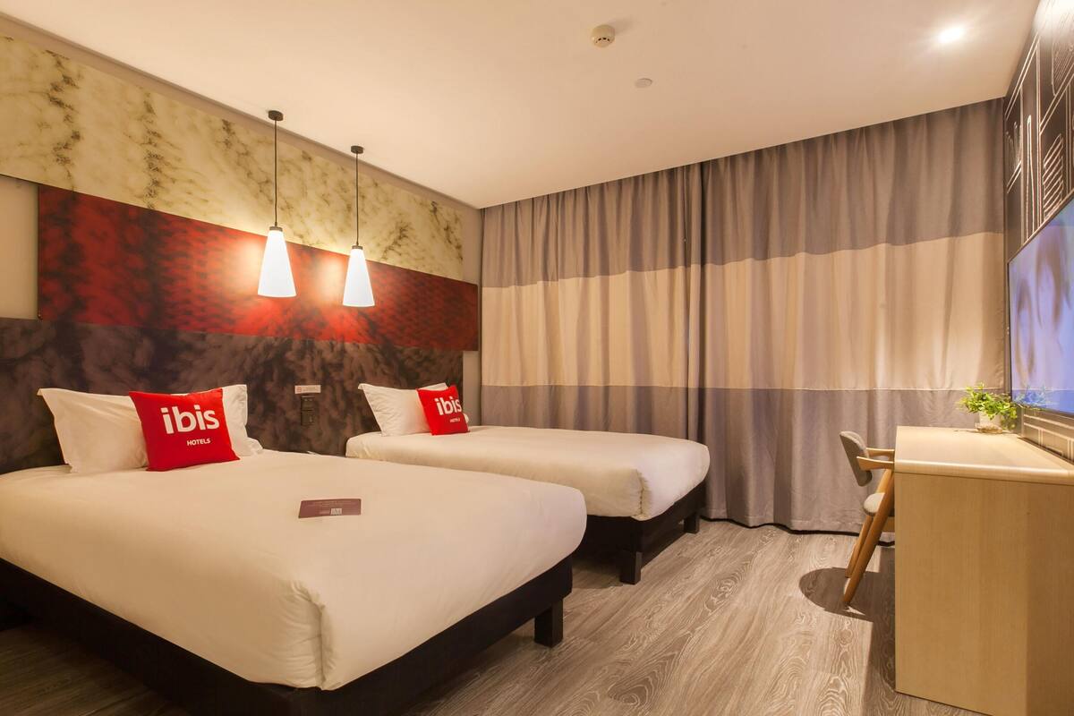 A hotel room with two beds, a desk, a TV, and a marble wall.