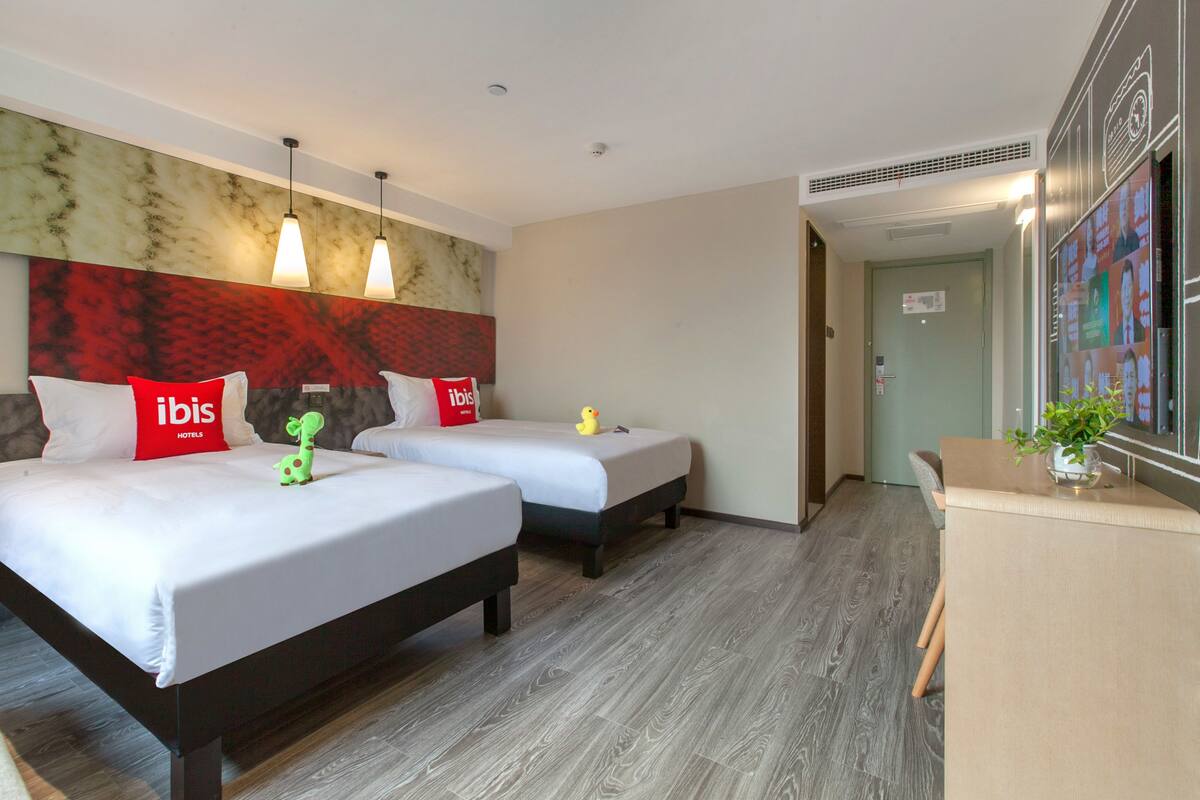 A hotel room with two beds, a minibar, and a view of the hallway.