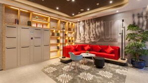 A modern lounge area with a red sofa, a coffee table, and a bookshelf with books and decorative items. - Ibis Wuhan Hubu Alley Hotel (Wuhan)