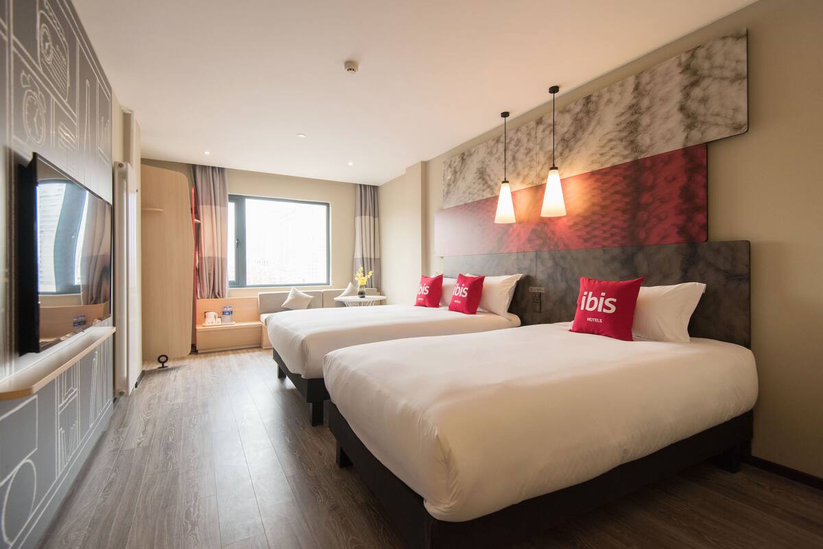 Une chambre d’hôtel avec deux lits, une grande fenêtre et un décor moderne.