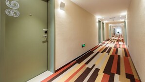A hotel hallway with a patterned carpet, a green door with a number, and a lighted exit sign. - Ibis Xian Xingqing Palace Park Hotel (Xi'an)