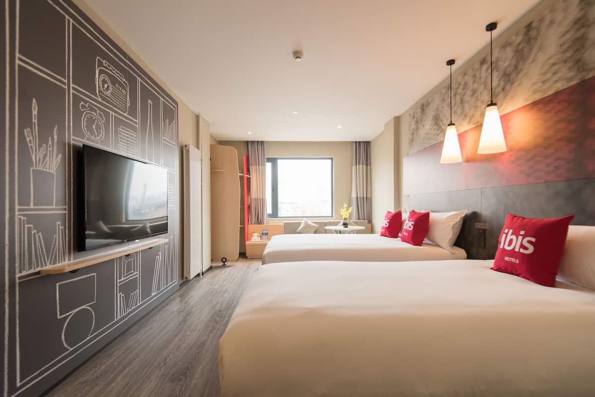 Une chambre d’hôtel avec deux lits, une télévision, un bureau et une fenêtre avec des rideaux.