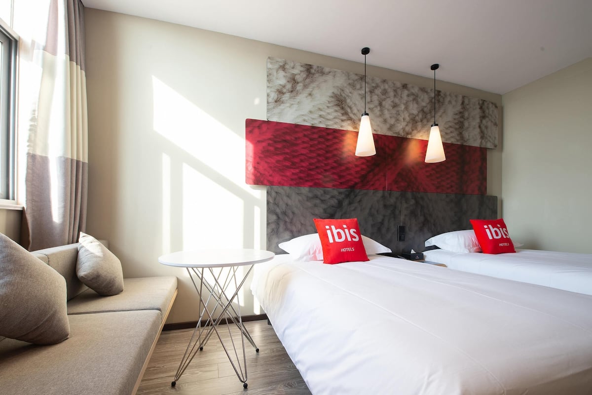 Ein Hotelzimmer mit zwei Betten, einem kleinen runden Tisch und einem Sofa.