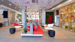A modern hotel lobby with a central seating area, a bookshelf, and a reception desk.