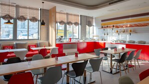 A modern dining area with red and white decor, multiple tables and chairs, and large windows with blinds.