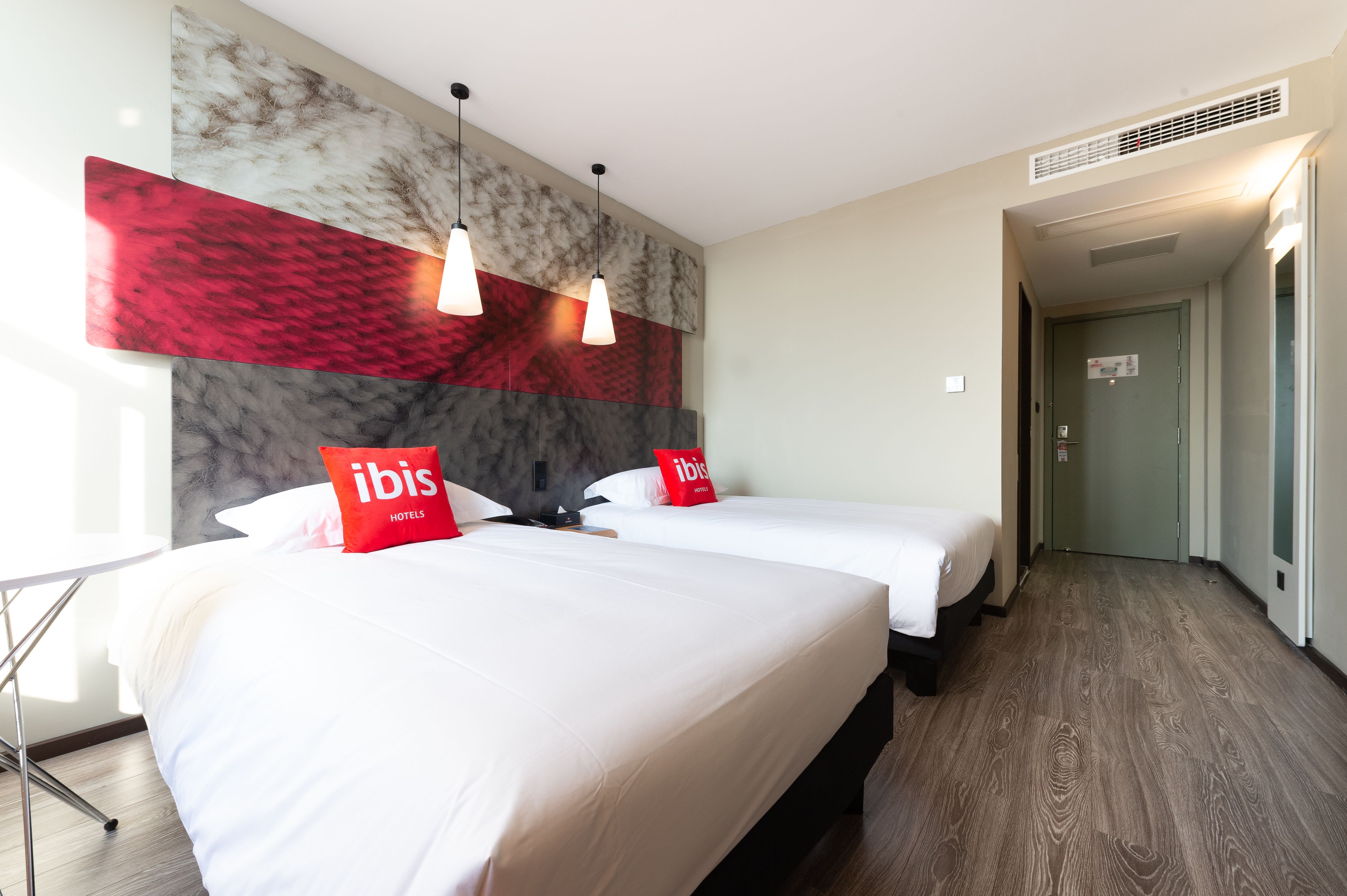 A hotel room with two beds, a modern wall design, and a hallway leading to the exit.