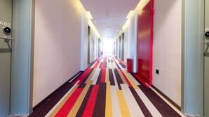 A hotel hallway with a striped carpet, doors numbered 602, and a red door on the right.