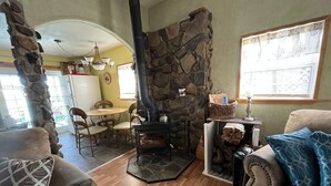 A cozy living room with a stone fireplace, wooden furniture, and a dining area with a chandelier. - Middle of town lodge style cottage (Silver City)