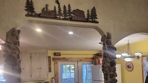 A rustic kitchen with stone pillars, wooden cabinets, a dining area with a table and chairs, and a view through the glass doors. - Middle of town lodge style cottage (Silver City)