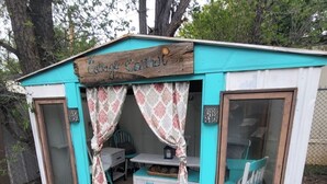 A small, rustic cabin with a wooden sign reading "Casa Corti". It features a cozy seating area with a table and chairs, and a large window on one side. - Middle of town lodge style cottage (Silver City)