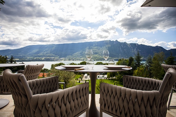 A table with two wine glasses and a plate, set against a scenic mountain view. - Hôtel L'Incomparable (Tresserve)