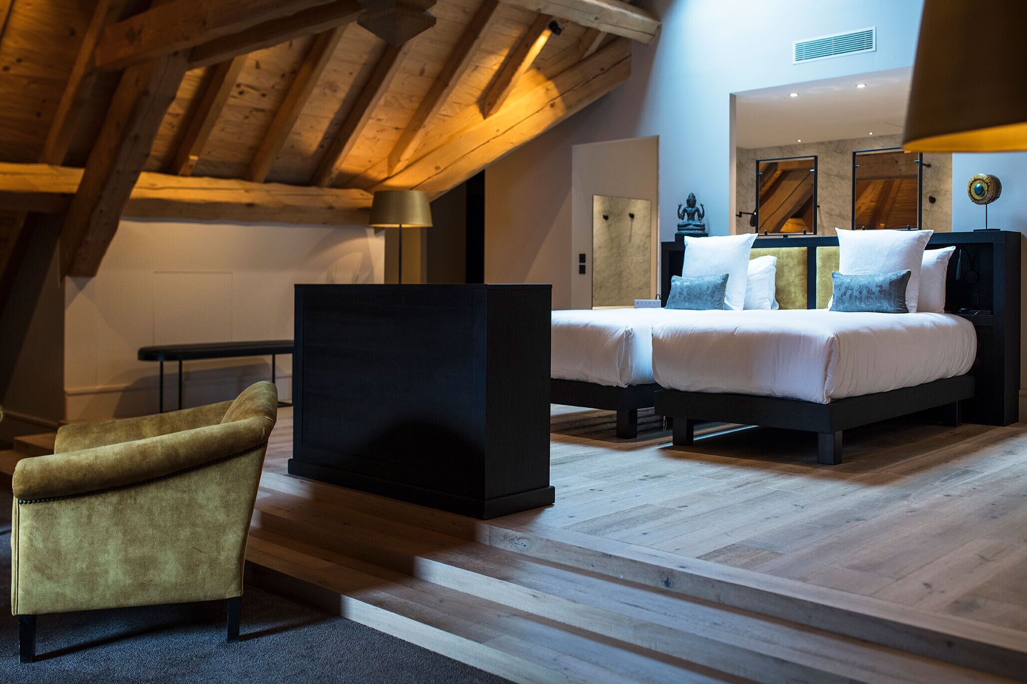 A modern bedroom with a loft-style ceiling, a bed with white bedding, a dark headboard, and a small armchair.