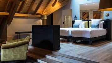 A modern bedroom with a loft-style ceiling, a bed with white bedding, a dark headboard, and a small armchair.