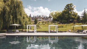 Una piscina con agua cristalina, rodeada de tumbonas y sombrillas, con un edificio grande al fondo.