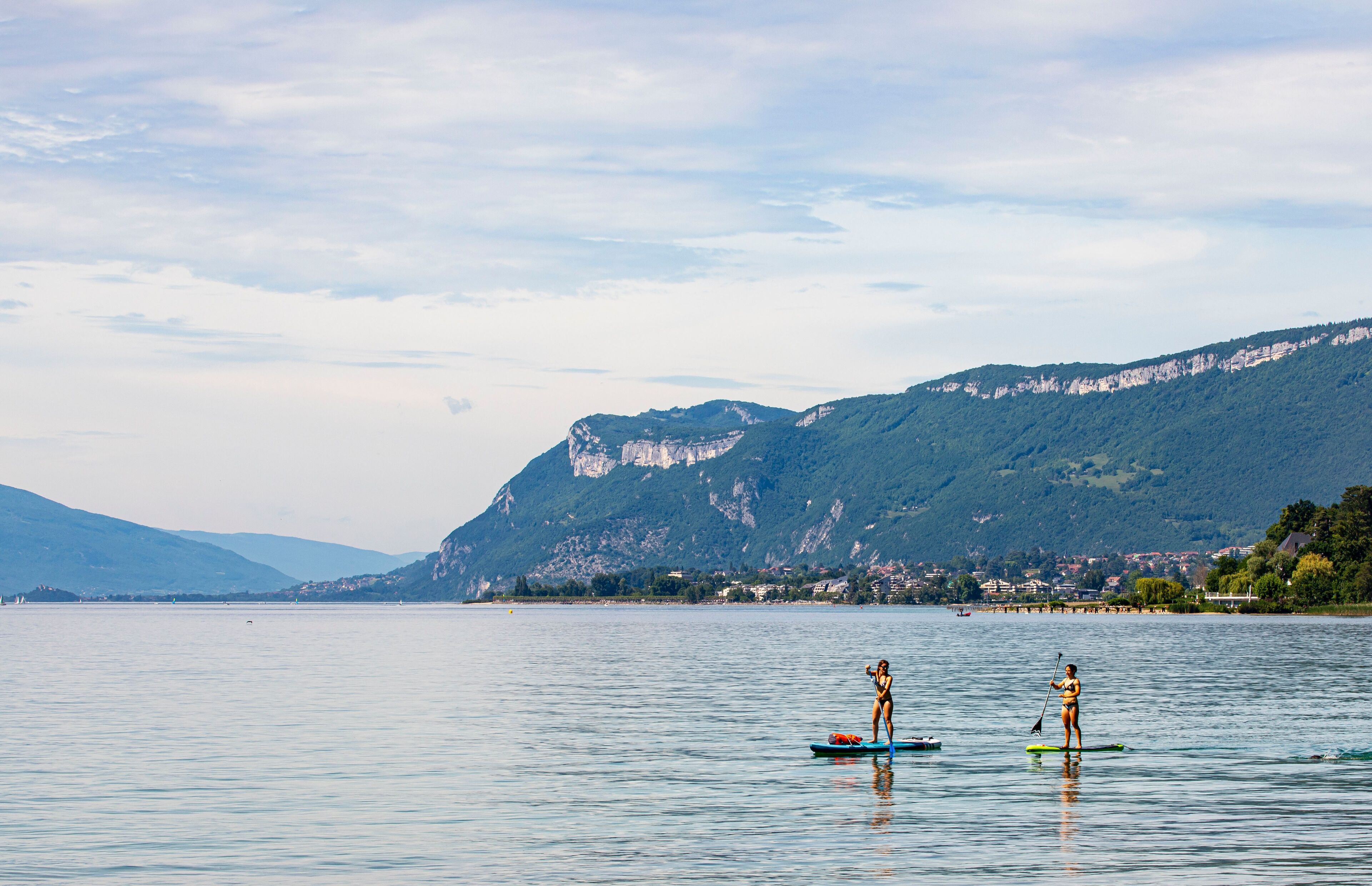 Un lago tranquillo con due tavole da paddleboard, una montagna sullo sfondo e una costa lontana con edifici.