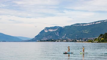 Un lago tranquillo con due tavole da paddleboard, una montagna sullo sfondo e una costa lontana con edifici.